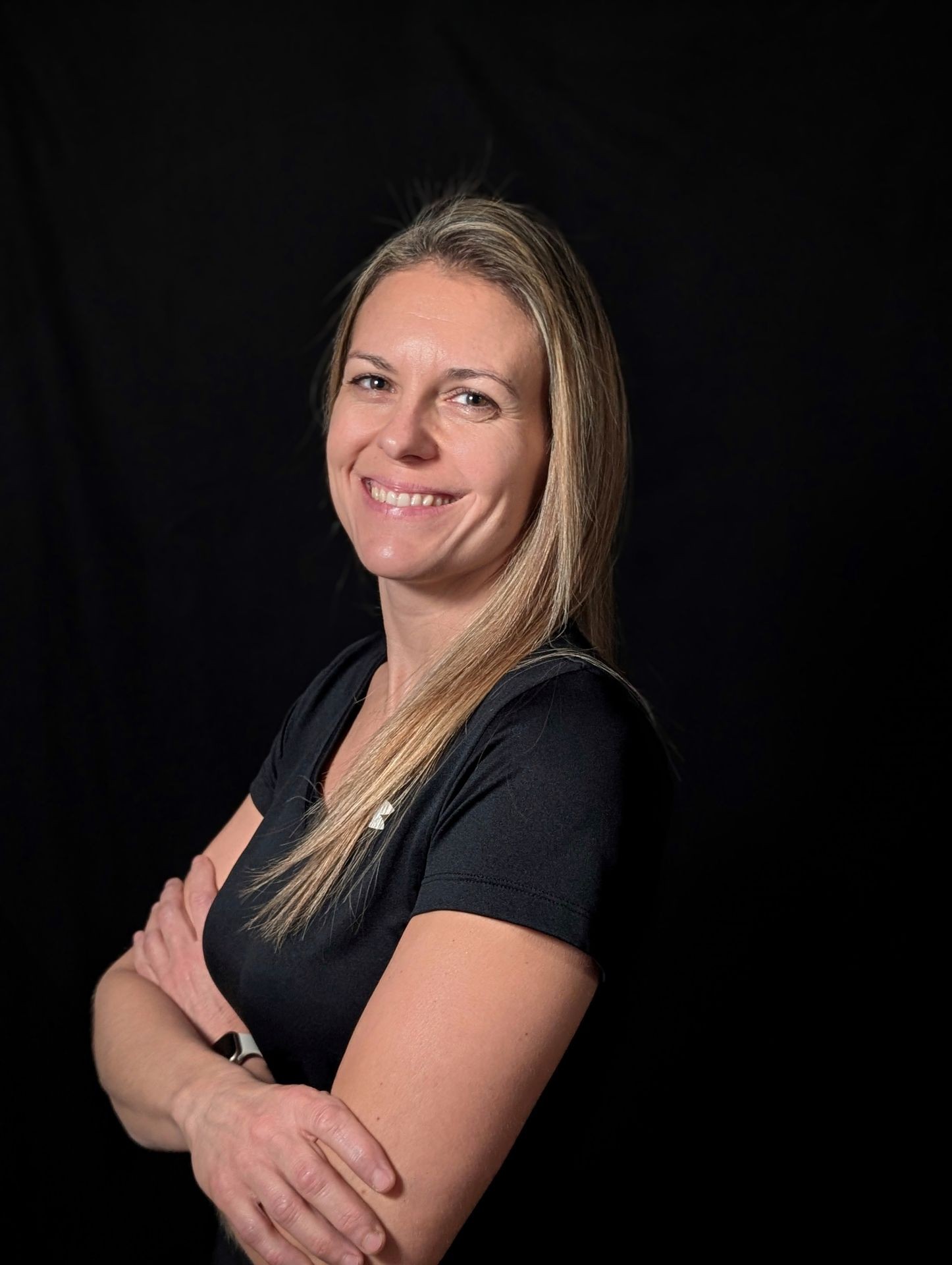 Smiling woman with long hair and a black shirt standing against a black background.